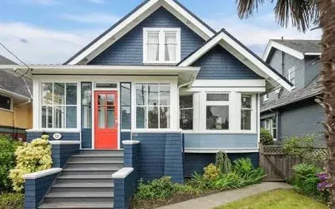 A blue character home with a steep gable, dormer and glassed-in front porch