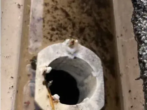 The downspout outlet in the base of a gutter, surrounded by silt and grit