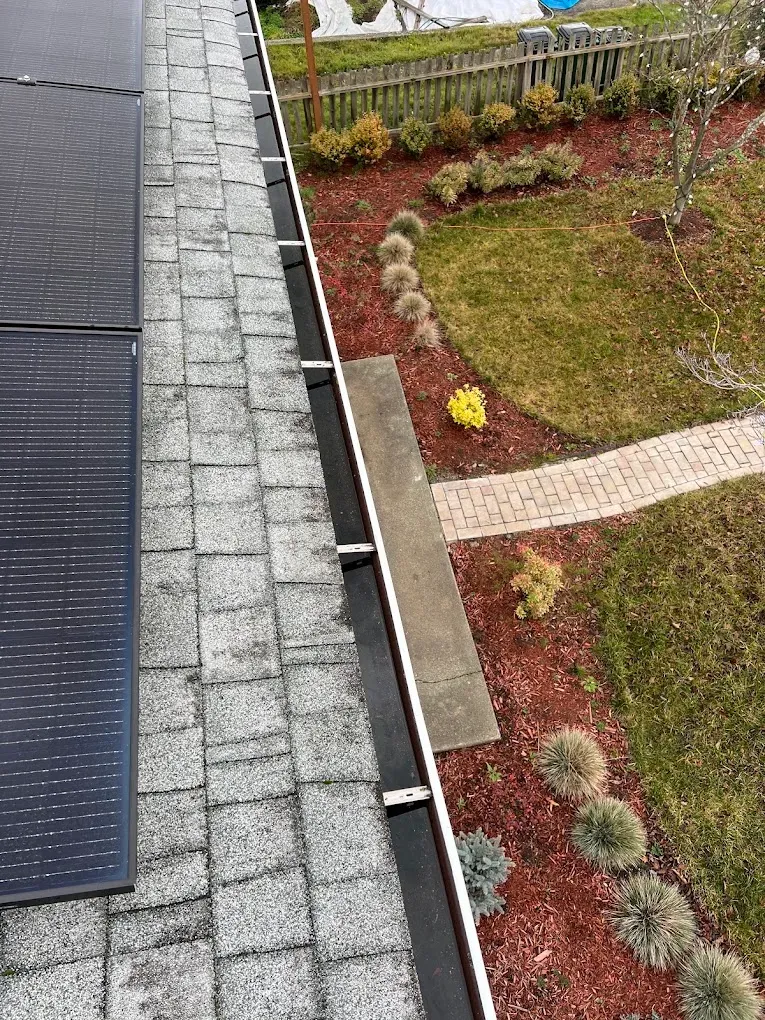 A clean gutter run beside roof solar panels, looking down over the garden