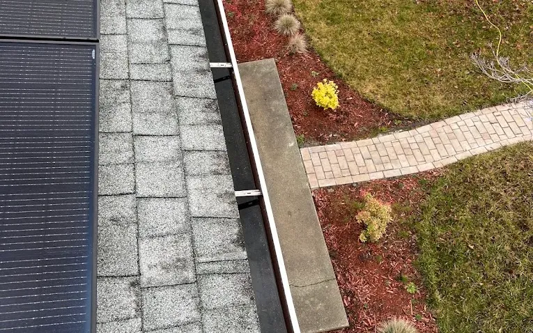 Looking along a clean dark gutter run beside rooftop solar panels