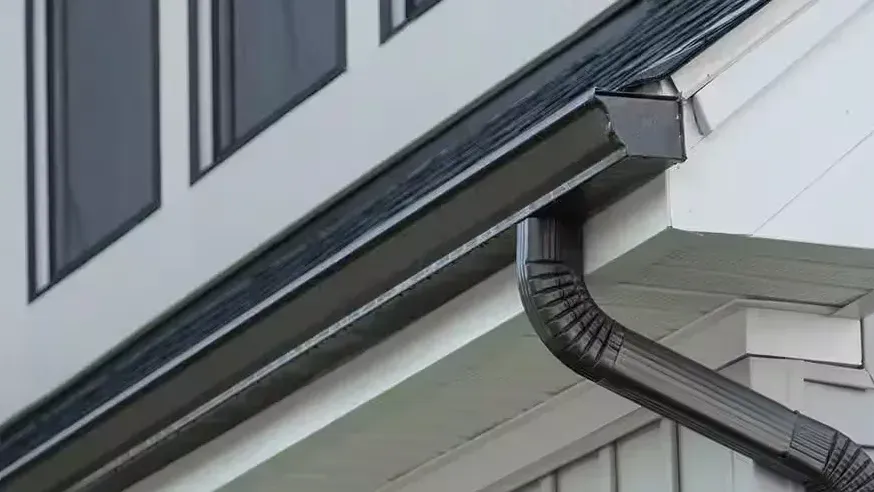A dark gutter run meeting its downspout elbow at the corner of the eave
