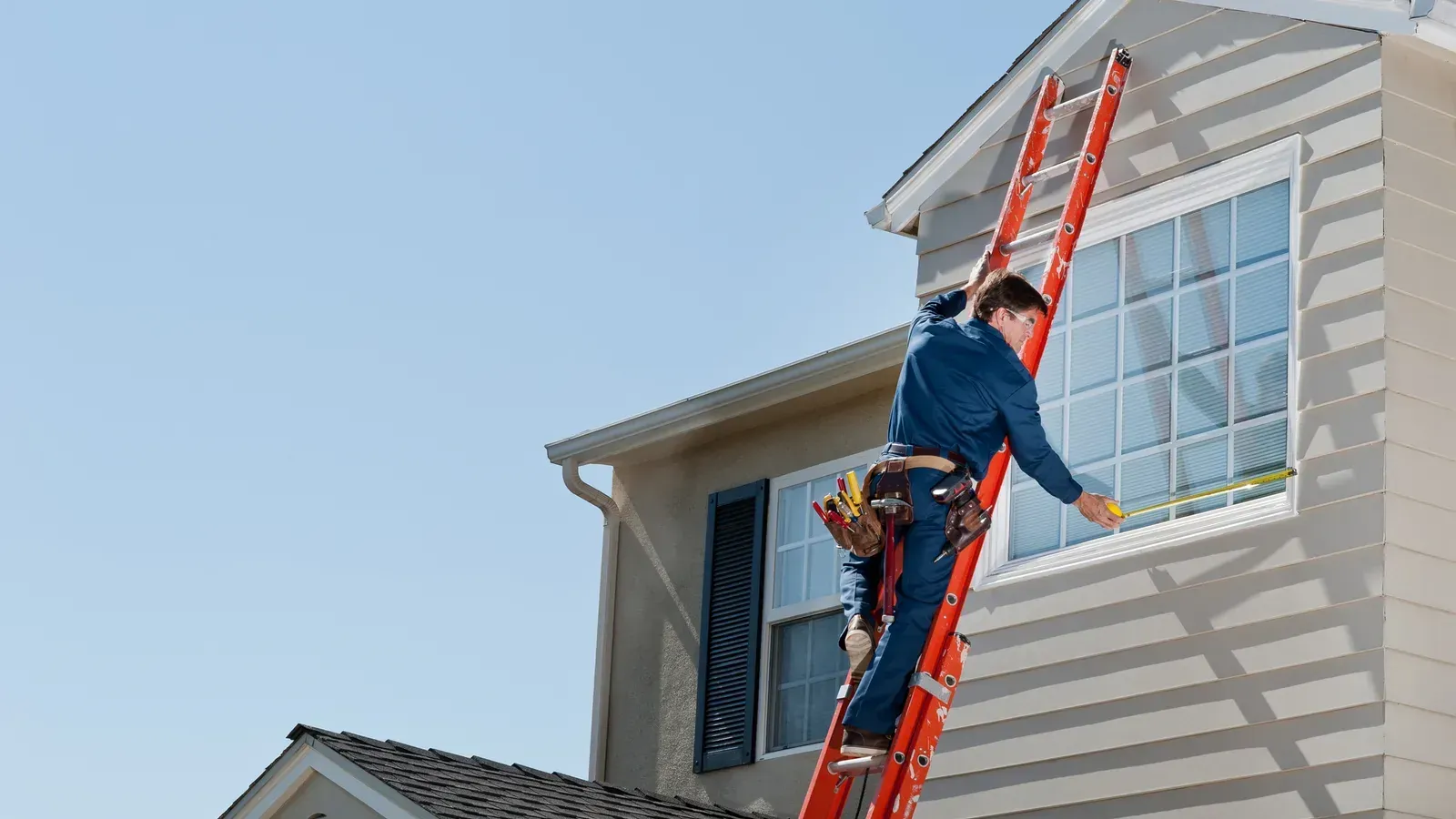 A tall orange extension ladder leaned against a house beneath the gable