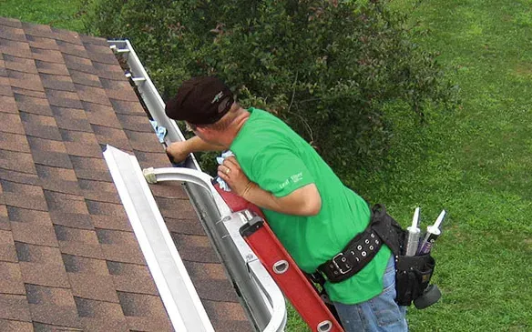 Working along a gutter from a ladder, sealant tubes in the tool belt